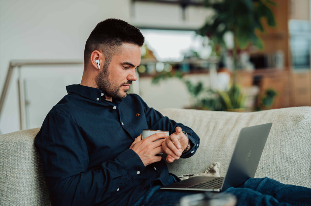 Photographie d'un homme assise dans un canapé et regardant des informations sur sa montre connecté, un café à la main.