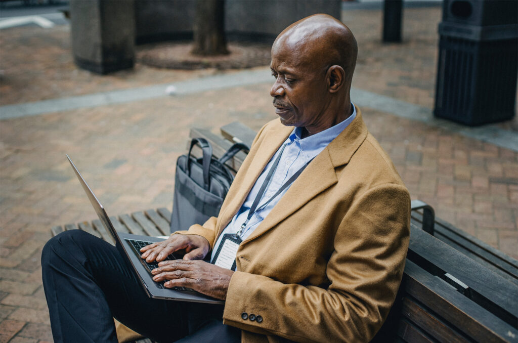 Photographie d'un homme travaillant sur son ordinateur portable en étant assis dehors sur un banc public. Sur son ordinateur il étudie le seuil de rentabilité de son business.